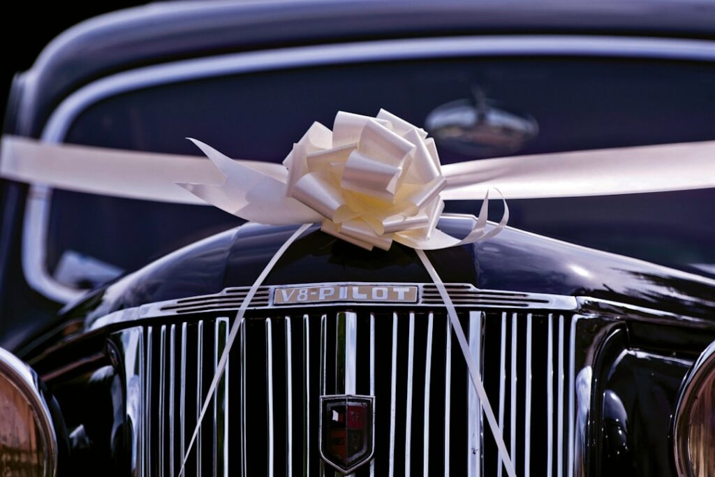Classic black wedding car decorated with a white satin bow and ribbon on the bonnet