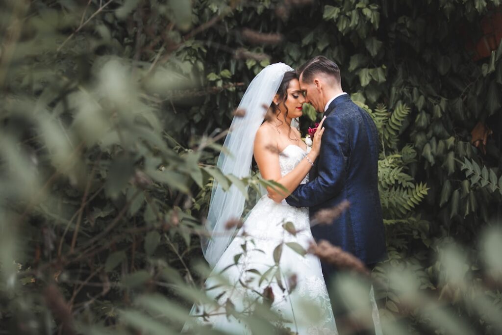 Bride and groom sharing a close, romantic moment framed by lush green foliage during outdoor wedding photography