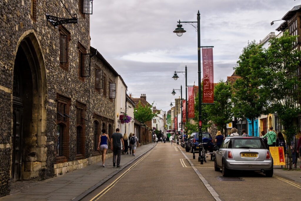 A quiet English town high street with stone buildings and parked cars, representing local Dorset coverage for wheelchair taxi services