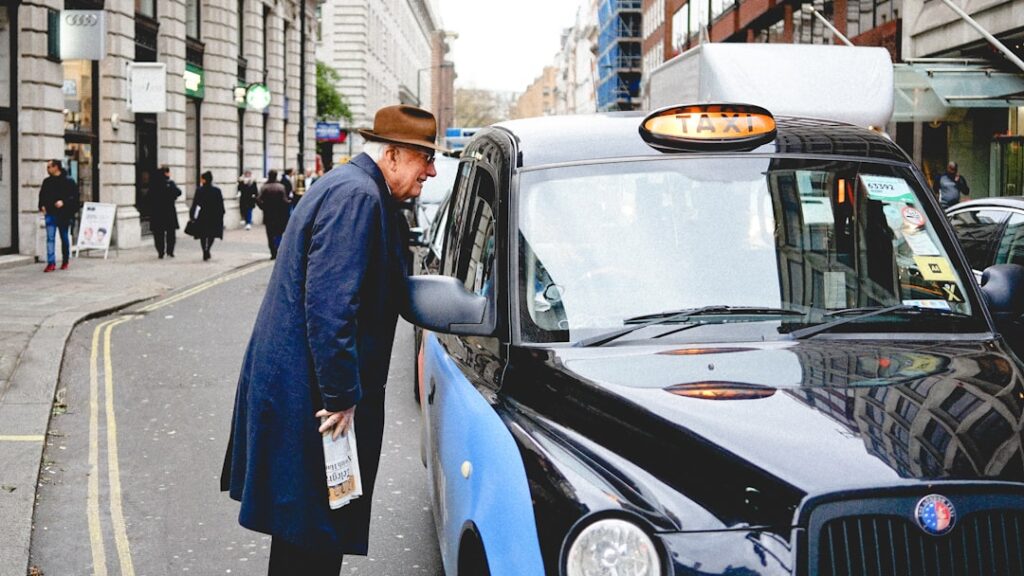 A passenger speaking to a licensed hackney carriage driver through the cab window on a British street, representing choosing a reliable wheelchair taxi provider