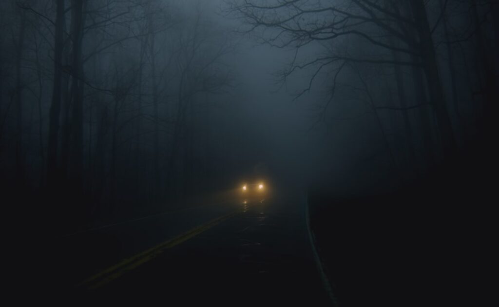 Car headlights on a dark foggy road at night — early morning and late night airport taxi transfers