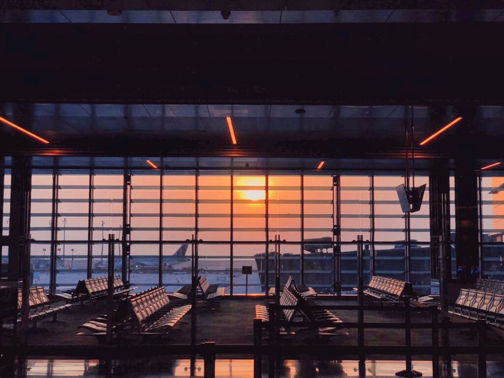 Empty airport terminal seating at dawn with a sunrise visible through large windows and a plane on the tarmac outside