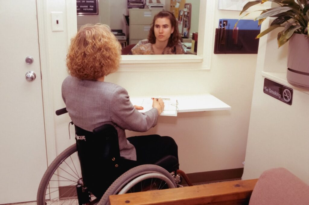 A wheelchair user at a reception desk checking in for an appointment, representing hospital and clinic visits made possible by accessible transport