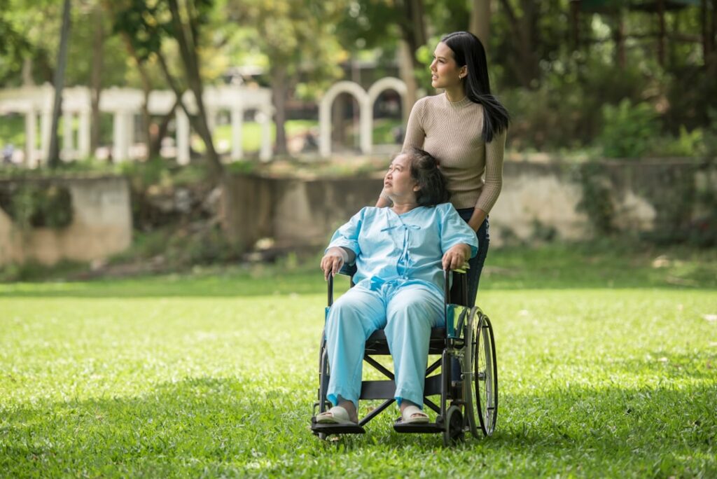 A carer assists an elderly woman in a wheelchair outdoors, illustrating the personal, respectful support provided by wheelchair cab drivers